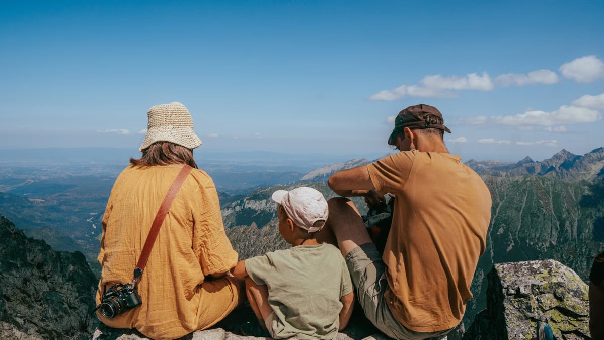 Family sitting on a rock, enjoying a panoramic view of the Tatra Mountains under clear blue skies.